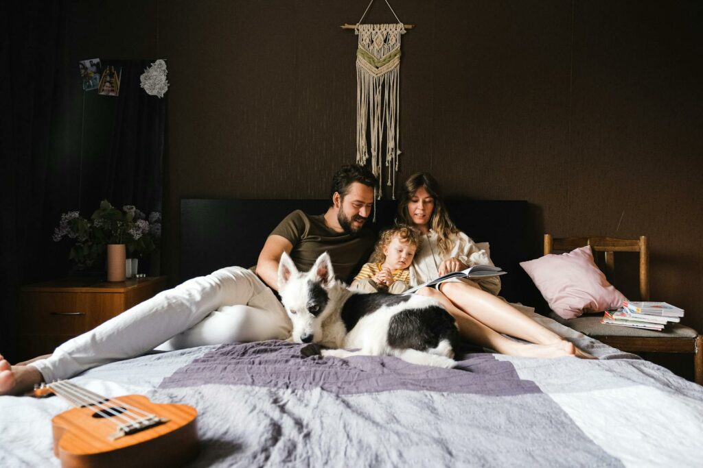 A family enjoys reading together with their pet dog in a cozy bedroom setting.